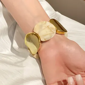 Primo piano di un bracciale elastico in acrilico oro e marmo indossato al polso.