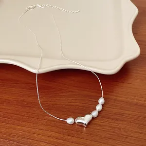 Primo piano di una collana con ciondolo a cuore argento e perle su vassoio in ceramica