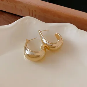 Close-up detail of minimalist golden water drop hoop earrings on a white plate