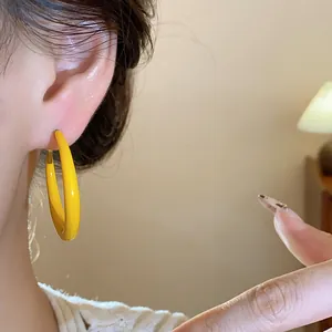 Close-up view of a bright yellow enamel hoop earring worn on an ear for a stylish look.