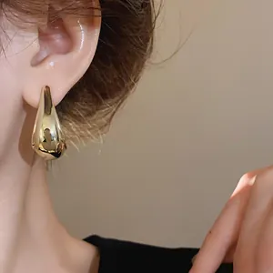 Elegant close-up shot of minimalist gold-plated water drop stud earrings worn on model's ear.