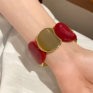 Primo piano di un braccialetto elastico in acrilico rosso e oro indossato sul polso