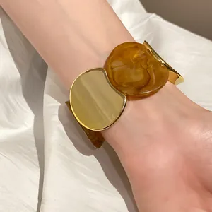 Dettaglio di un bracciale elastico con maglie in metallo dorato e acrilico ambra.
