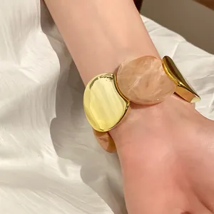 Vista dettagliata di un bracciale elastico in acrilico e metallo dorato indossato al polso.