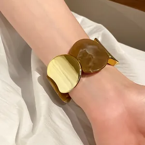 Dettaglio del bracciale elastico a cerchi grandi in oro e acrilico marmorizzato.