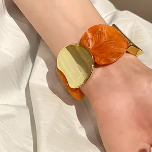 Dettaglio di un bracciale elastico in acrilico marmorizzato arancione e metallo oro.