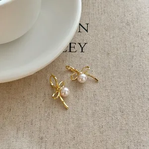 Detail view of gold bow earrings with elegant pearl center on textured background