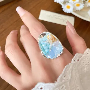 Close-up of a French retro ring featuring blue beads, shell, and pearl on hand.