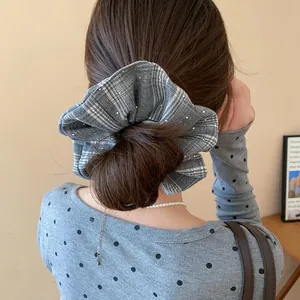 Detailed view of a grey plaid scrunchie with rhinestones worn on a stylish hair bun