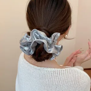 Close-up view of silver metallic ruffled hair scrunchie on a messy low bun hairstyle
