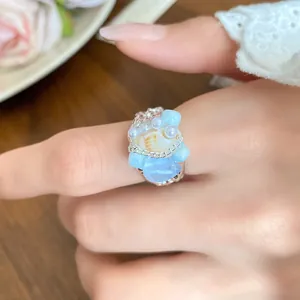 Close-up of French vintage shell and light blue stone beaded ring on index finger