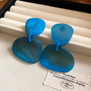 Macro view of blue irregular marbled geometric drop earrings on a beige display tray