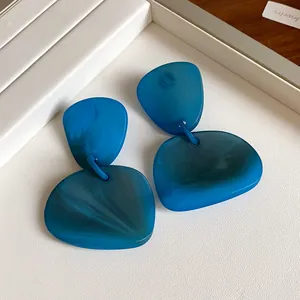 Close-up of irregular blue marbled resin dangle earrings on white display tray