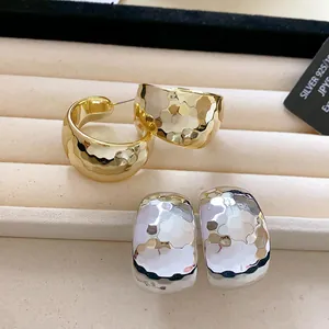 Detailed view of gold and silver C-shaped earrings with hammered metal texture