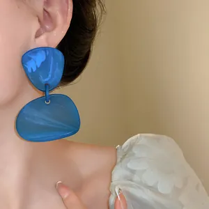 Detailed view of large irregular blue marbled resin drop earrings worn by a model