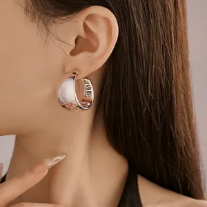 Macro detail showing the hammered texture of silver C-shaped hoop earrings on a model
