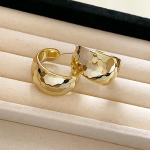 Macro view of minimalist gold hammered C-shaped hoop earrings on a soft jewelry display