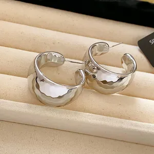 Detailed view of chunky silver-tone C-shaped hoop earrings featuring a hammered metal texture.