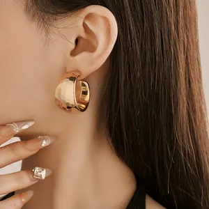 Close-up detail of a minimalist gold C-shaped earring with a hammered texture finish.