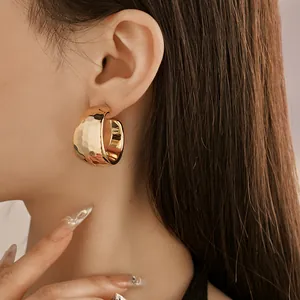Detailed close-up showing elegant gold C-shaped earrings with hammered texture on a model