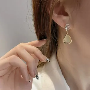 Close-up view of elegant gold-tone teardrop earrings with cat's eye stone details on ear