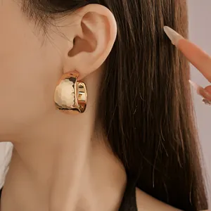 Detailed close-up showing the hammered texture of gold C-shaped hoop earrings on ear