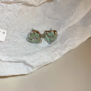 Detailed view of vintage heart-shaped stud earrings with pale green cat-eye stones