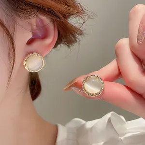 Close-up of elegant gold-rimmed cat's eye stone stud earrings worn by a model