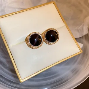 Close-up of retro gold-toned round stud earrings with dark cat's eye stones on a white cushion