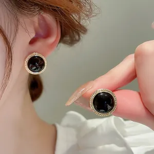 Close-up detail of vintage round black cat-eye stud earrings with gold textured border
