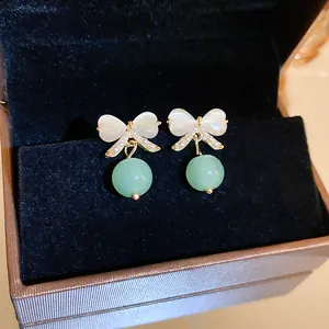 Macro detail of elegant bow-shaped cat's eye stud earrings with round green bead pendants