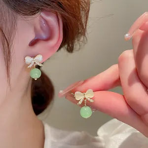 Detailed close-up of retro silver needle earrings with a green cat's eye stone bowknot design.
