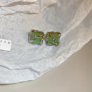 Detailed view of square green cat's eye stone stud earrings with silver wavy frame
