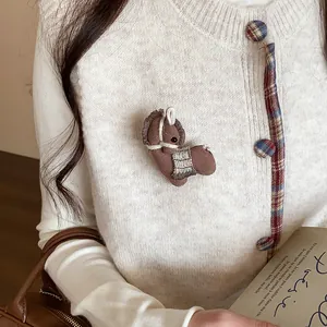 Gros plan d'une jolie broche cheval tricotée marron sur un cardigan blanc doux