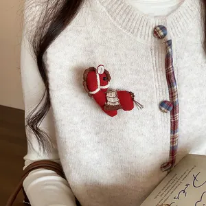 Gros plan d'une broche poney tricotée rouge faite main épinglée sur un pull en maille blanc.
