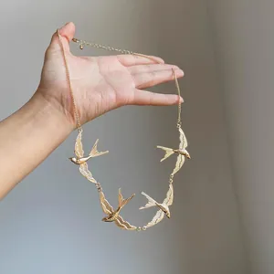 Detailed close-up of a gold swallow necklace held by hand showing intricate wing textures