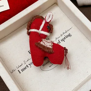 Vue détaillée d'une broche cheval en tissu rouge faite main dans un coffret cadeau blanc