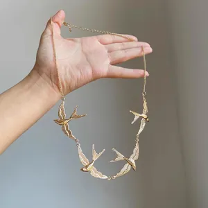 Detailed view of a gold swallow bird necklace held by hand showing intricate textures