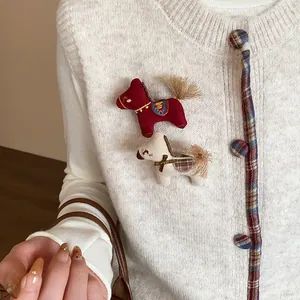 Gros plan de deux broches cheval en tricot rouge et crème épinglées sur un cardigan.