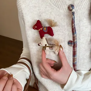 Vue détaillée de broches de cheval en tissu faites main sur un gilet en tricot blanc.
