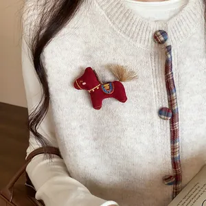 Détail d'une broche en forme de cheval rouge épinglée sur un gilet en maille blanc