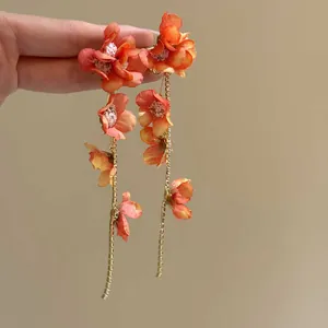 Close-up of elegant orange fabric flower long drop earrings with gold tassels
