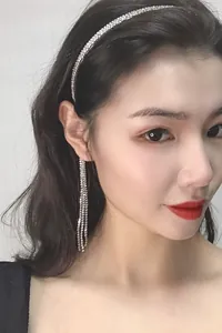 Gros plan du modèle portant un élégant serre-tête à pompons en strass et boucles d'oreilles