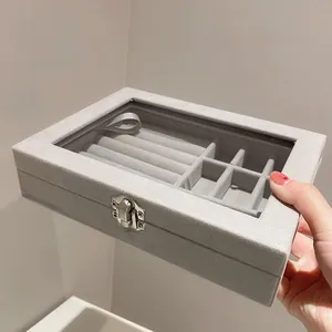 Détail d'une boîte à bijoux en velours gris avec couvercle transparent et emplacements bagues