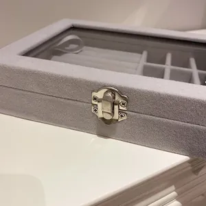 Vue rapprochée d'une boîte à bijoux en velours gris avec couvercle en verre et fermoir en argent.