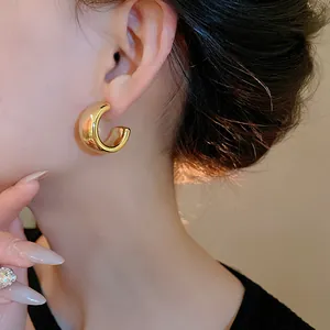 Primo piano di una modella che indossa orecchini a cerchio dorati a forma di C.