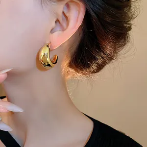 Primo piano di un orecchino a perno dorato a forma di C a goccia indossato da una donna.
