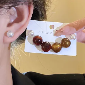 Close-up of colorful resin pearl earrings in white and amber tones shown on a display card.