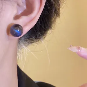 Detailed view of a minimalist round iridescent resin earring shown being worn on an ear