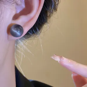 Close-up of a round grey resin stud earring with cat-eye effect worn on ear